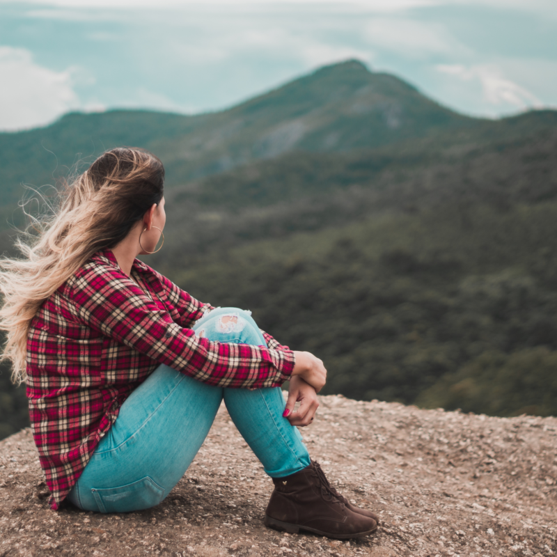A woman sitting on a rocky viewpoint overlooking green mountains.