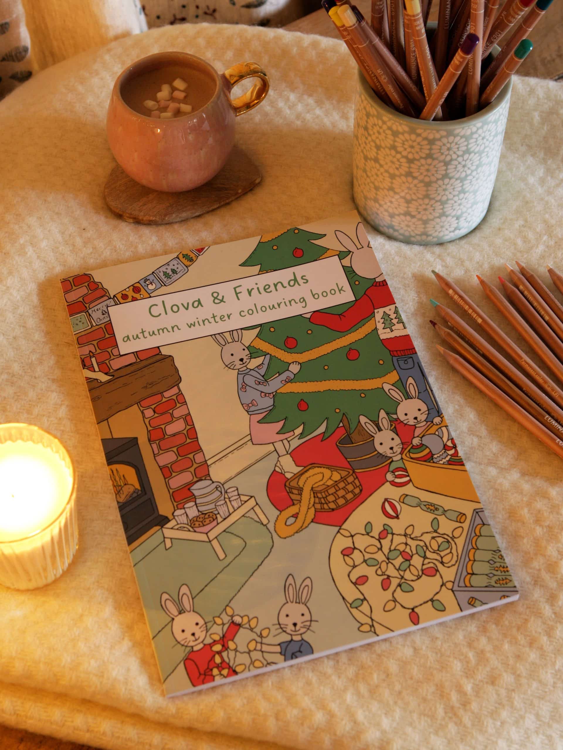 Clova and Craft winter colouring book beside coloured pencils, a mug and a candle.
